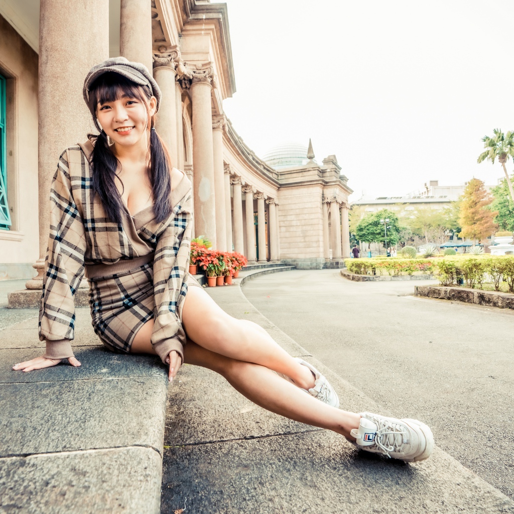 Улыбающаяся азиатка в кепке сидит на ступеньках 