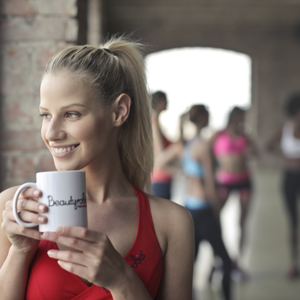 Улыбающаяся спортивная девушка с чашкой кофе у окна