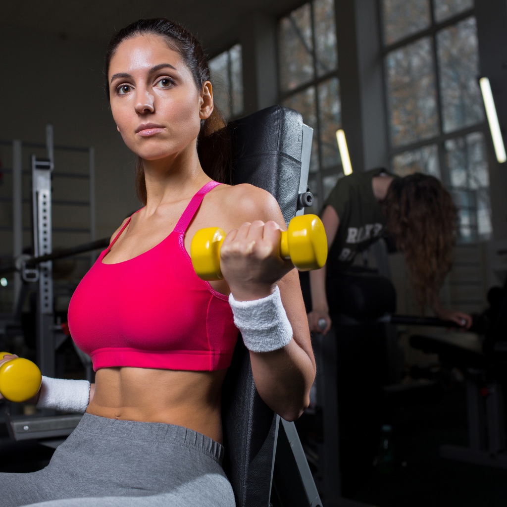 Спортивная девушка качает руки желтыми гантелями в спортзале