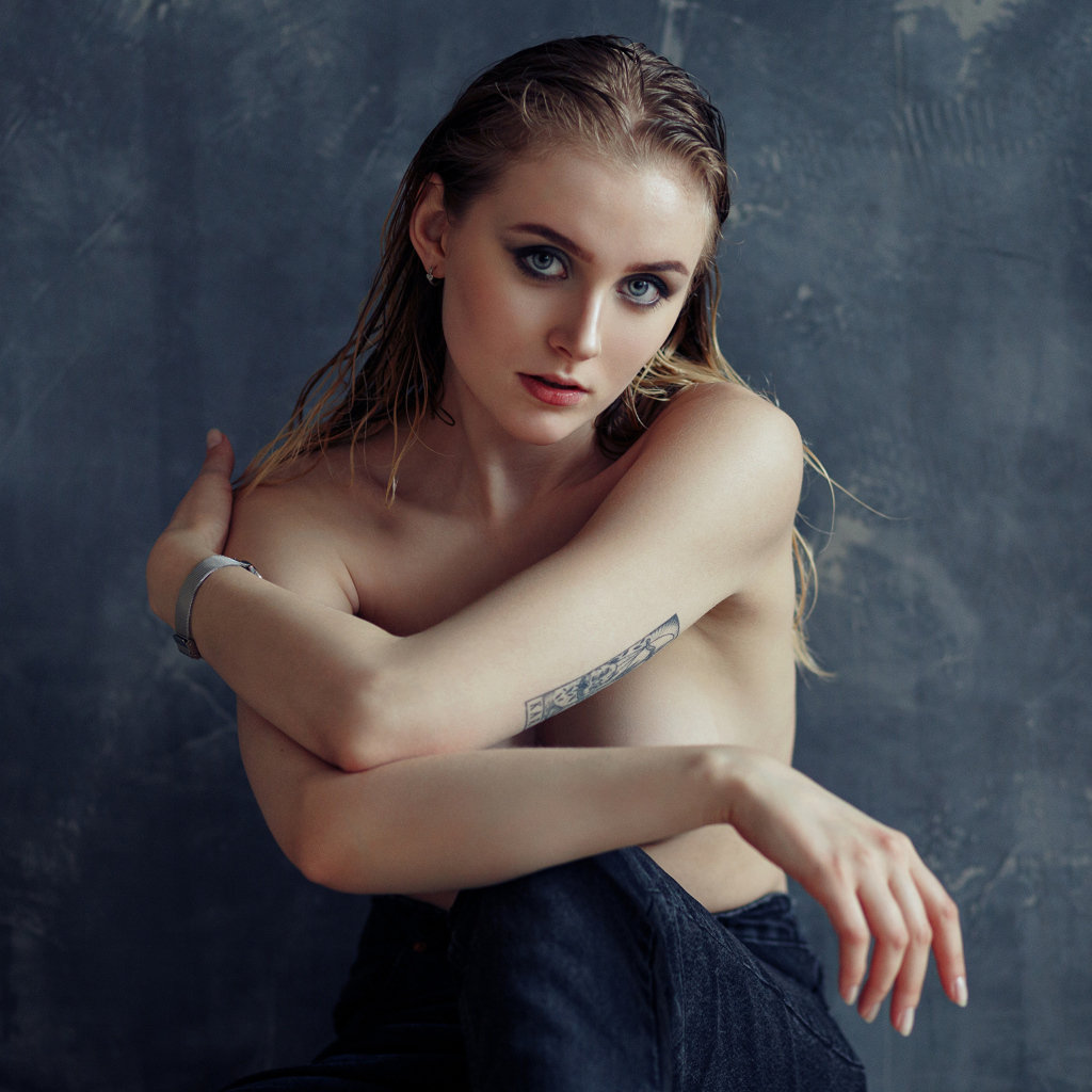 Нежная девушка с татуировками на теле сидит у стены