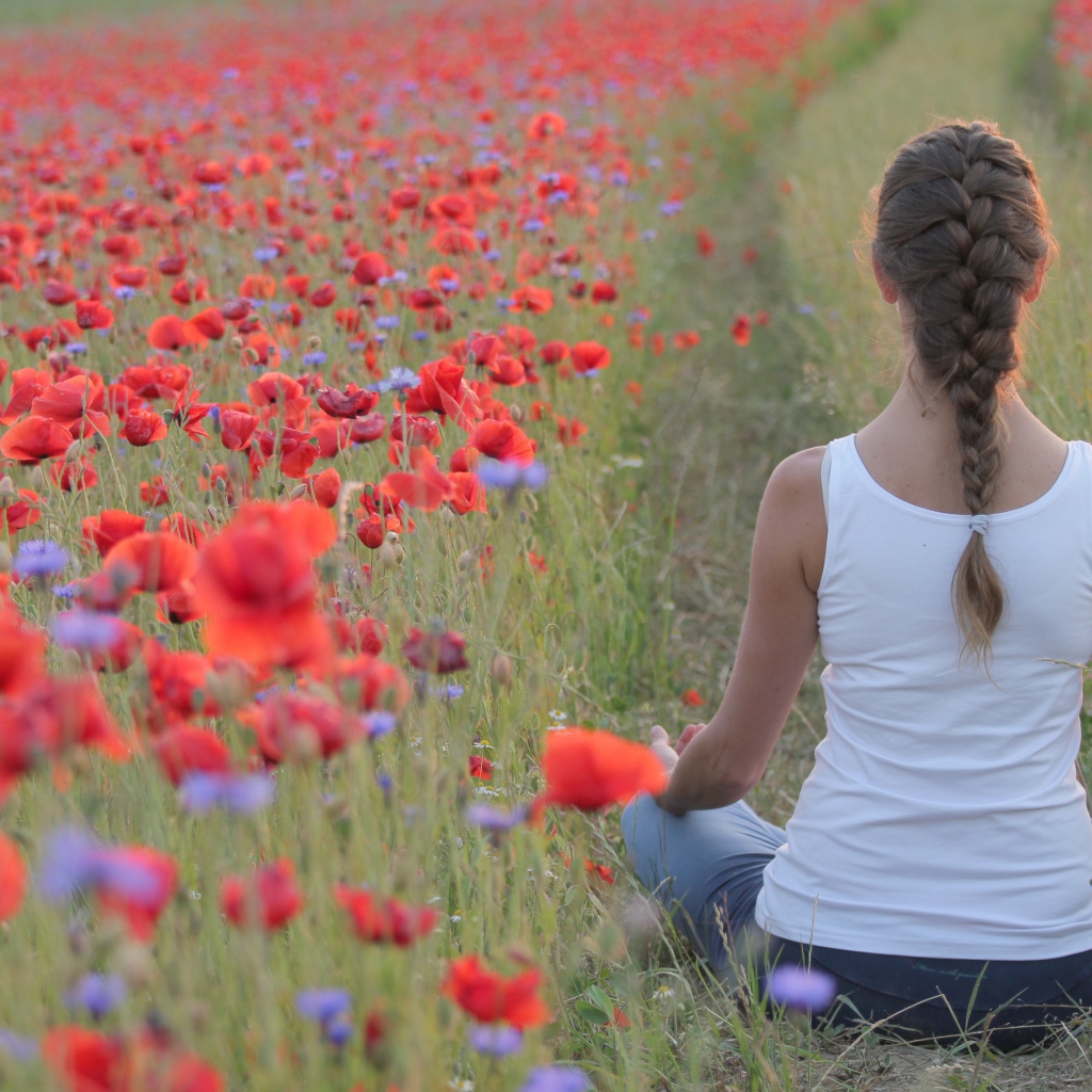 Молодая девушка медитирует на поле с красными маками
