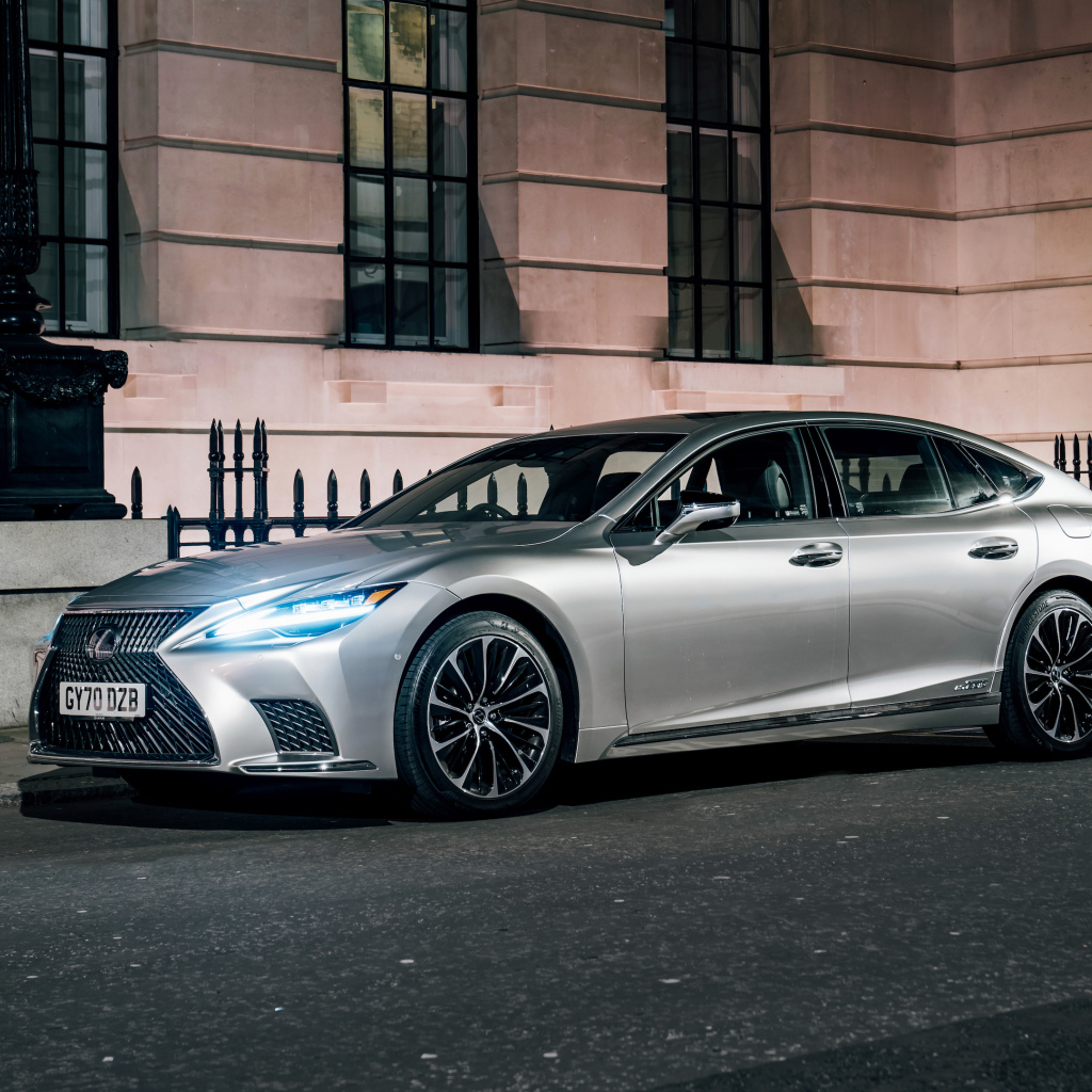 Серебристый автомобиль Lexus LS 500h 2021  года с включенными фарами