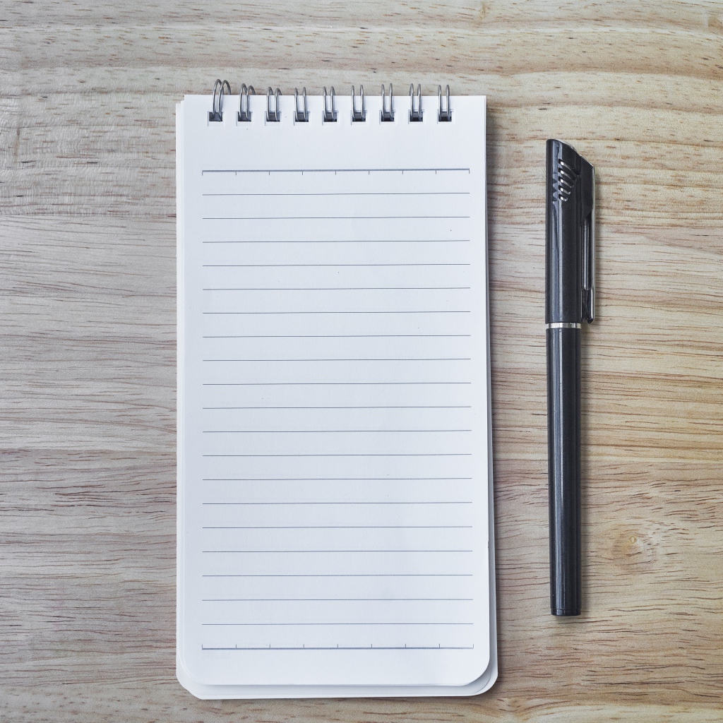 Авторучка и блокнот лежат на деревянном столе