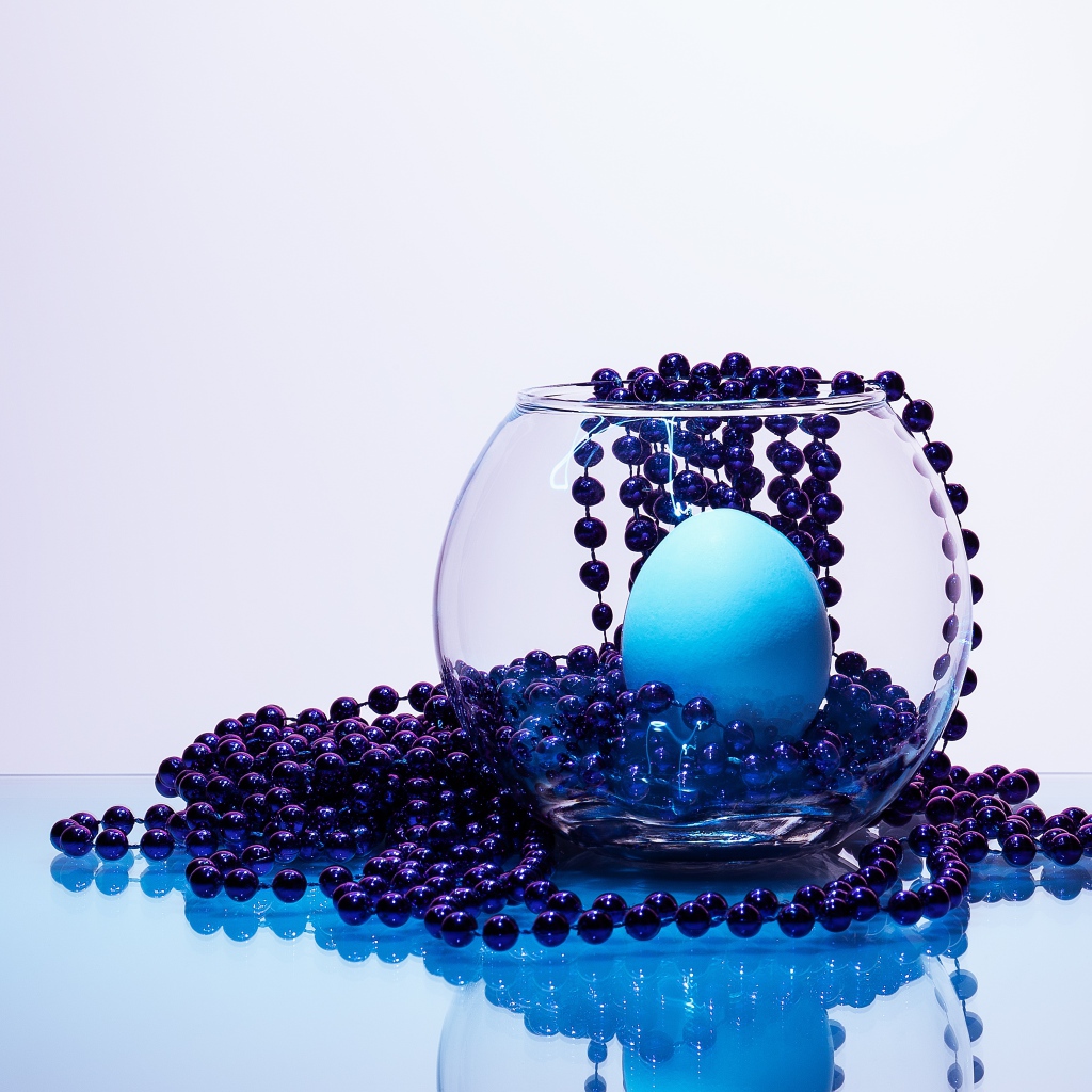 Blue beads on a table with a glass vase and an egg