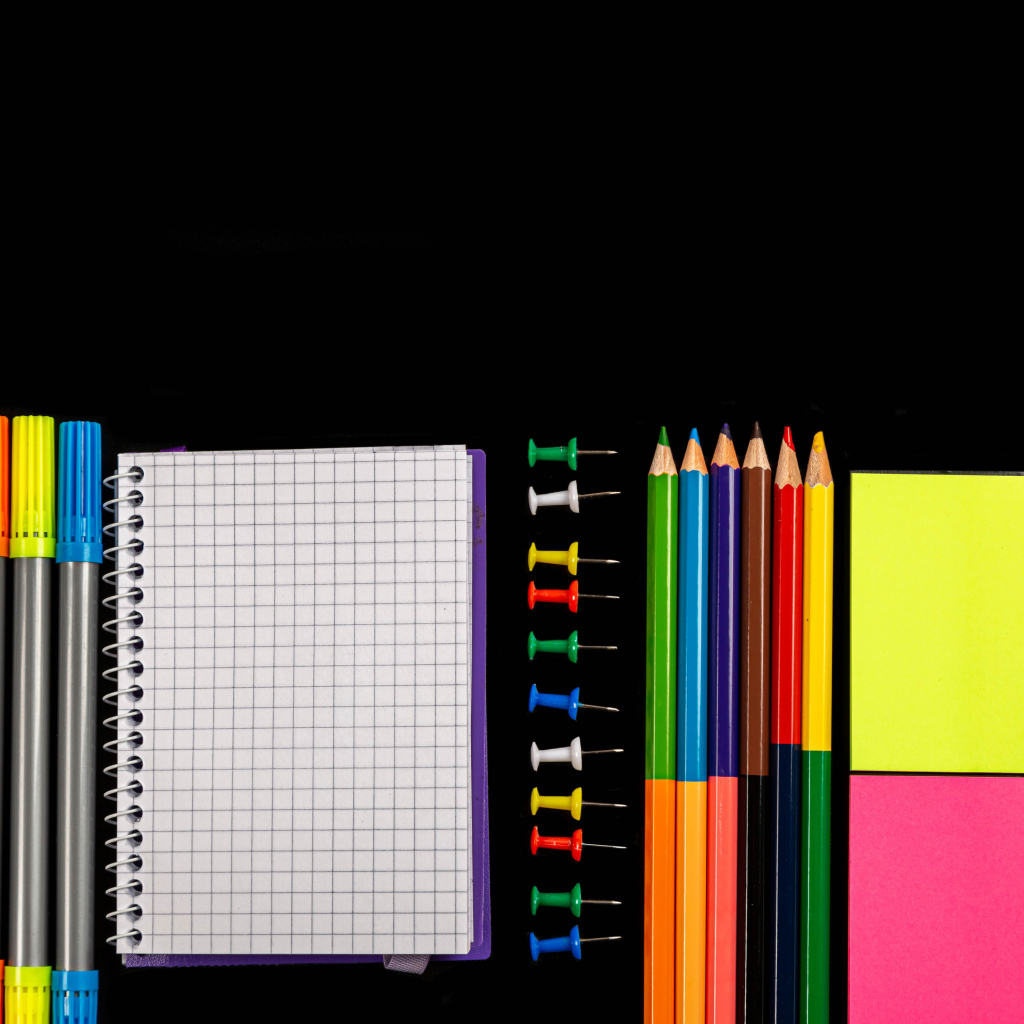 Фломастеры, карандаши, тетрадь и кисточки на черном фоне 