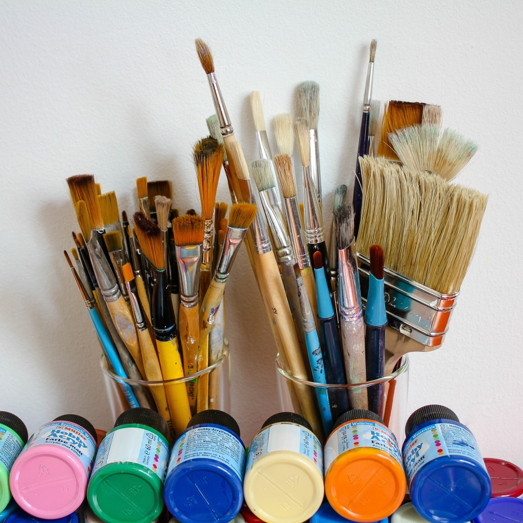 Много кисточек и разноцветные краски у стены
