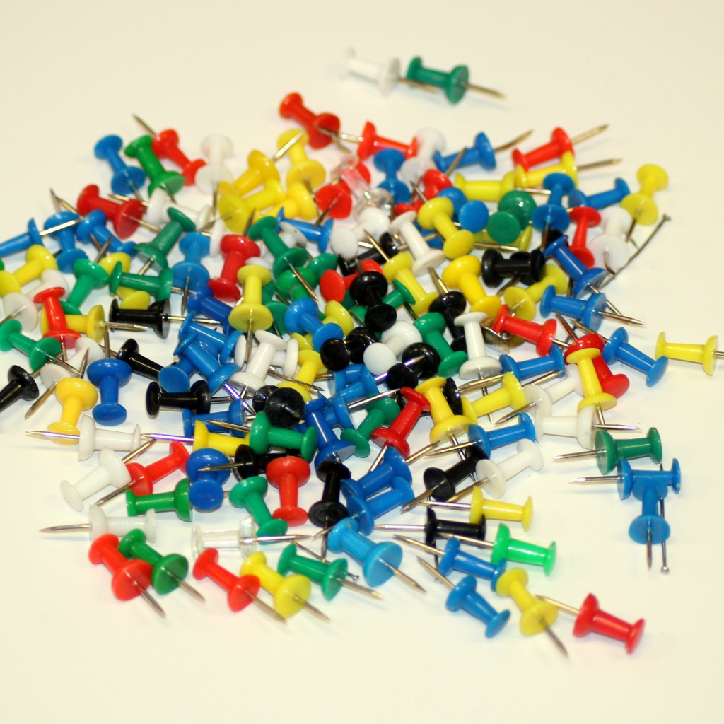 Разноцветные канцелярские гвозди на белом фоне