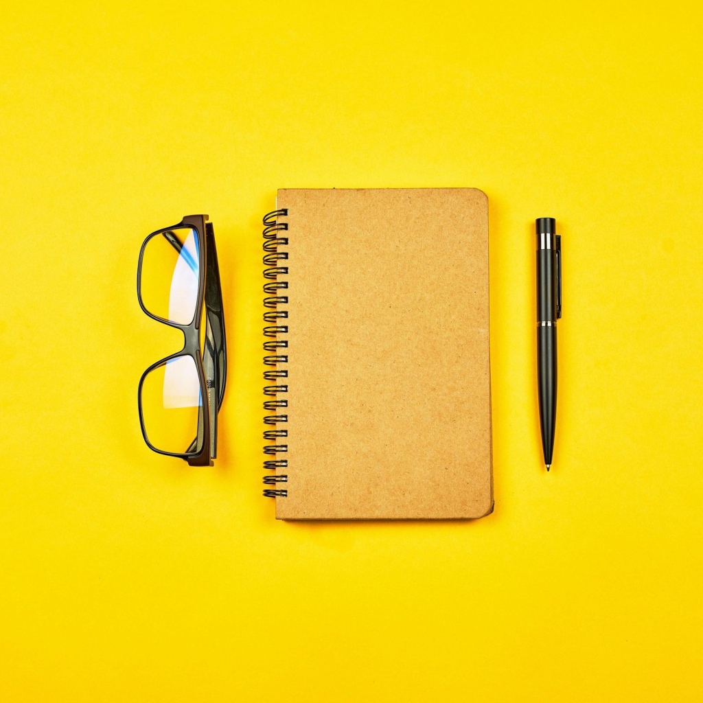 Блокнот, очки и ручка на желтом фоне