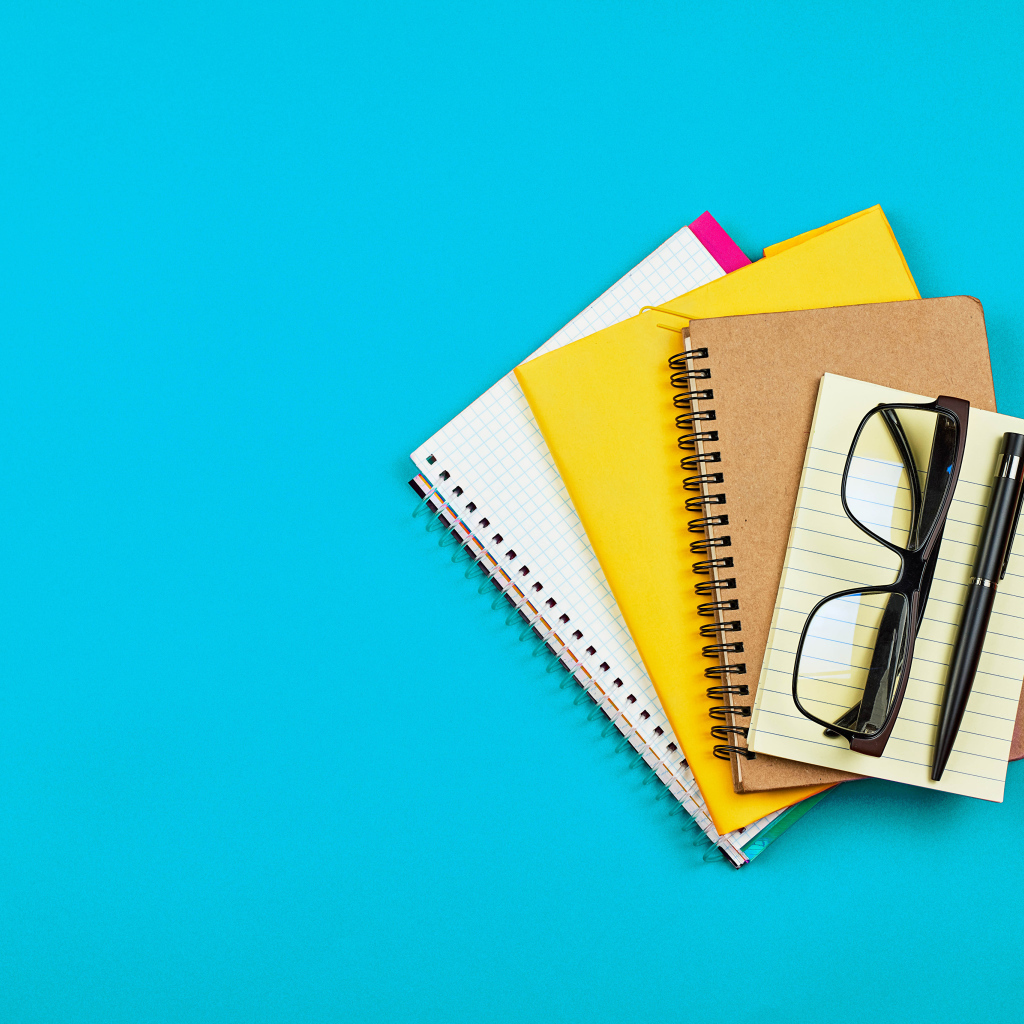 Блокноты, очки и ручка на голубом фоне