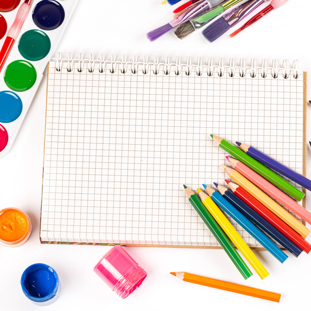 Карандаши, краски и тетрадь на белом фоне 