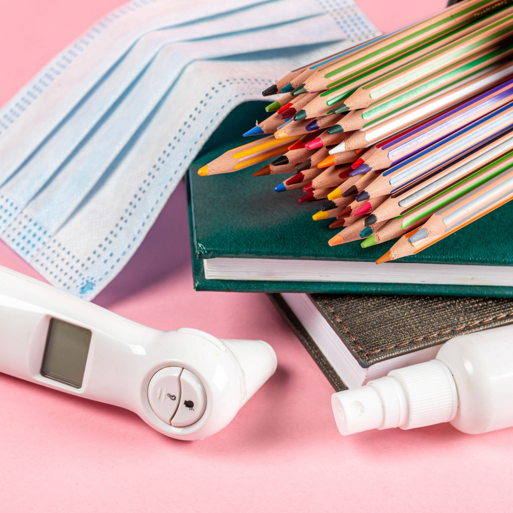 Карандаши, градусник, маска и блокнот на розовом фоне 