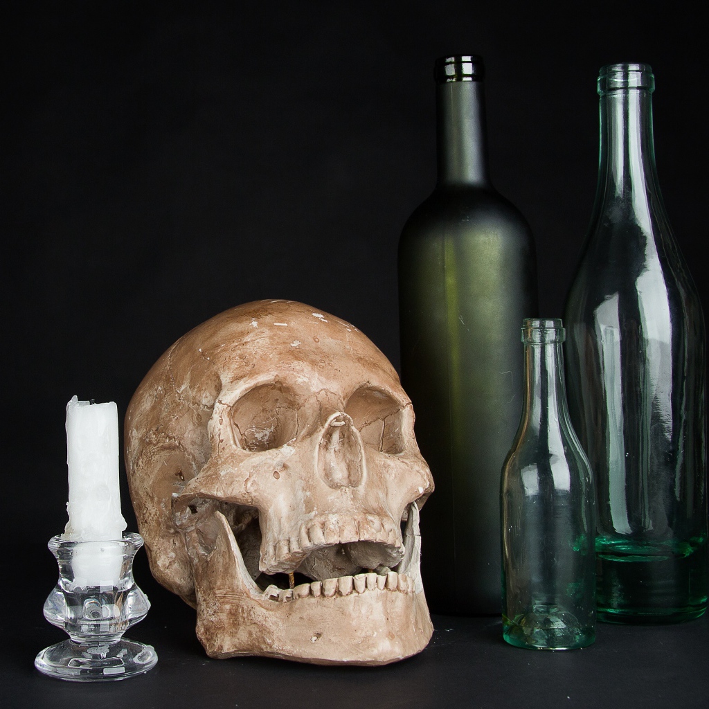 Череп, пустые бутылки и свеча на черном фоне