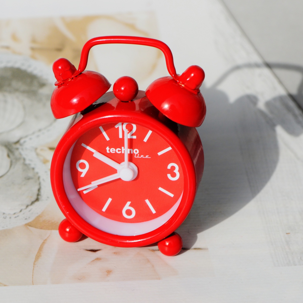 Маленький красный будильник стоит на столе 