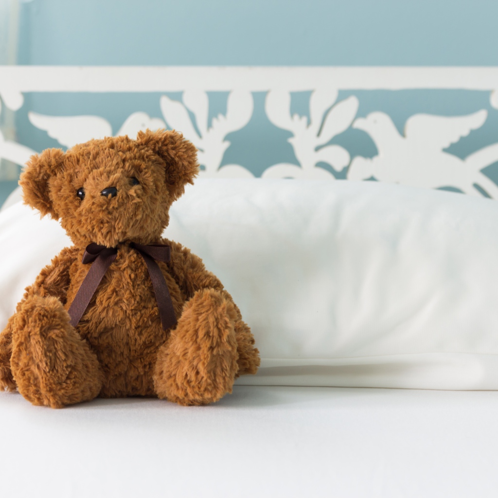 Игрушечный медвежонок сидит на белой постели