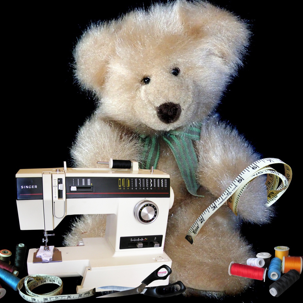Игрушечный медвежонок со швейной машинкой на черном фоне 