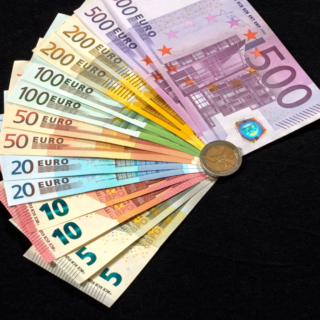 Пачка купюр евро с монетой на черном столе 