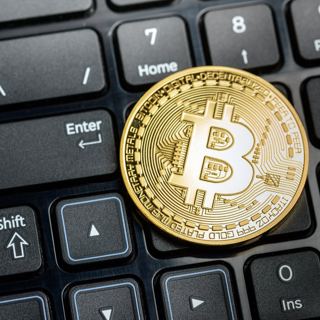 Золотая монета биткоин на черной клавиатуре