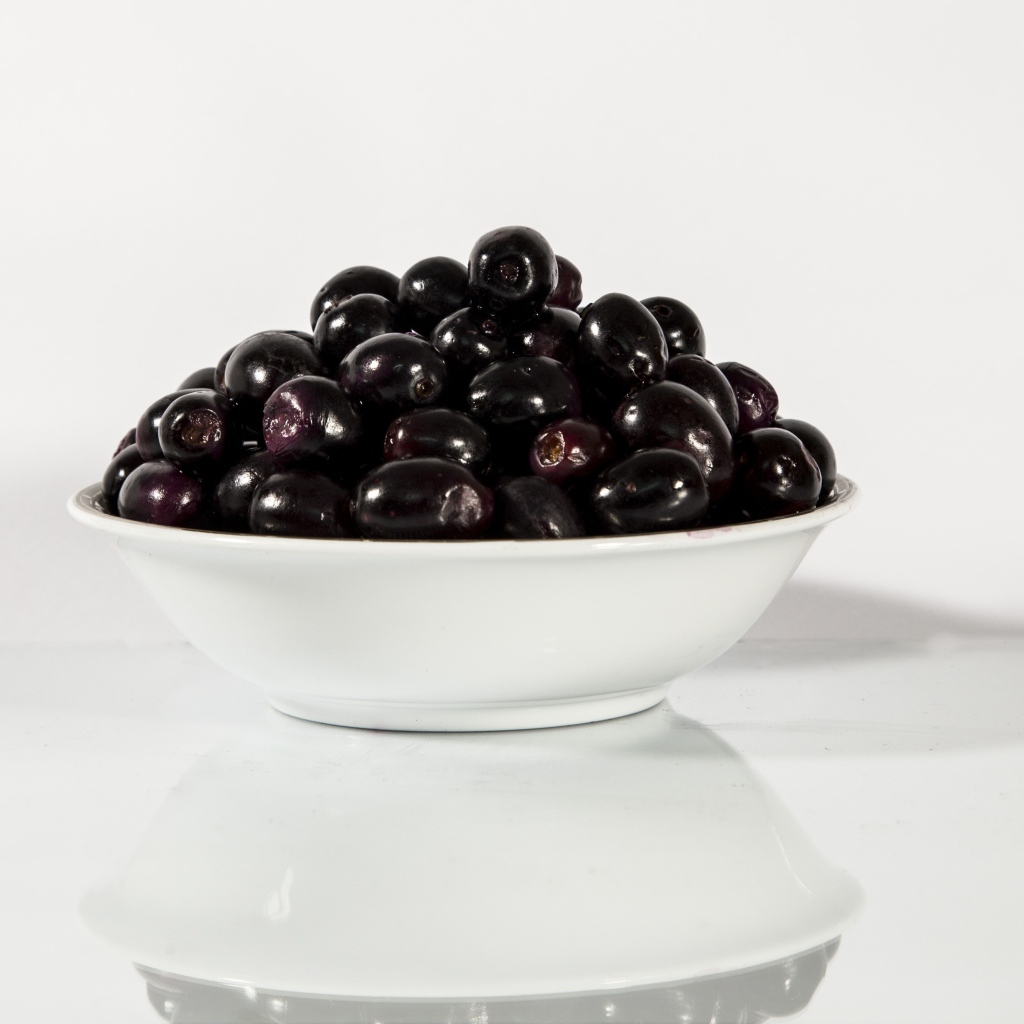 Черные оливки в белой тарелке отражаются в поверхности