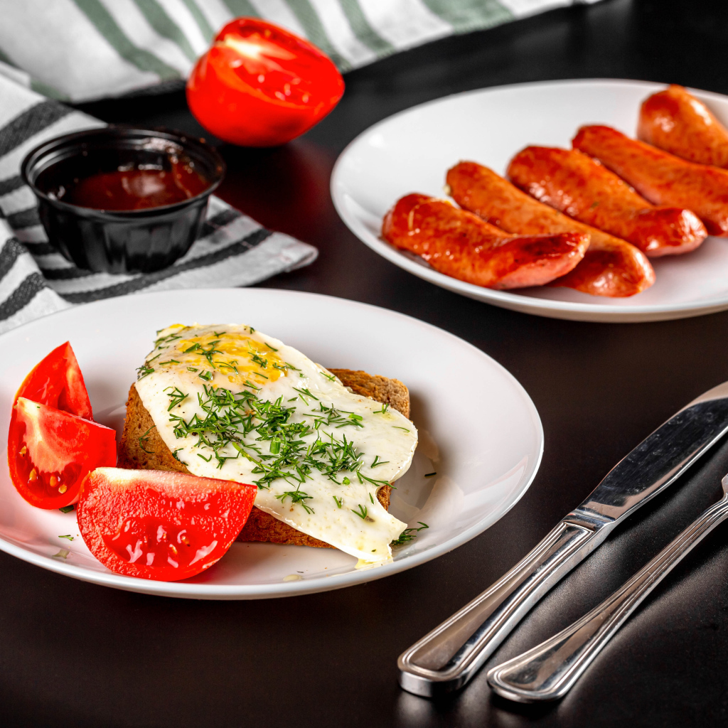 Хлеб с яичницей и помидорами на тарелке с сосисками