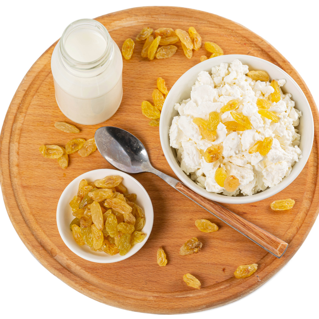 Творог с изюмом и молоком на доске на белом фоне 