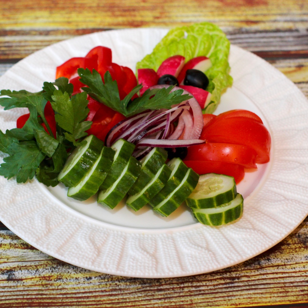 Свежие овощи на белой тарелке на деревянном фоне