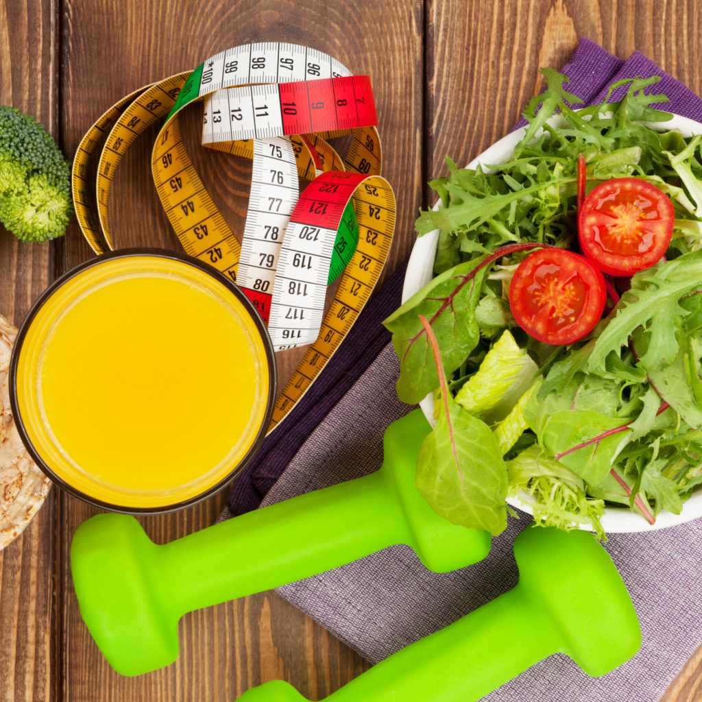 Салат из зелени на столе с соком и гантелями