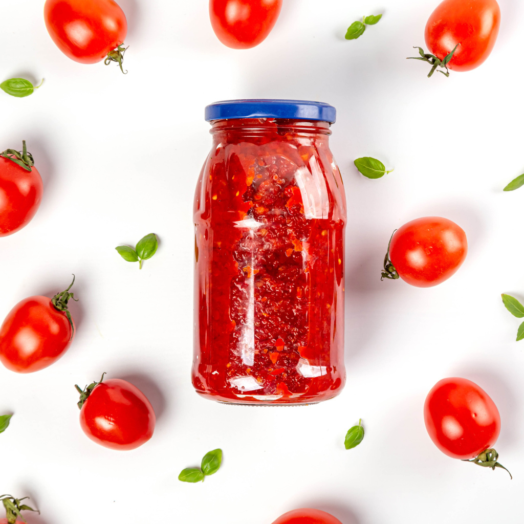 Банка аджики на белом фоне с помидорами