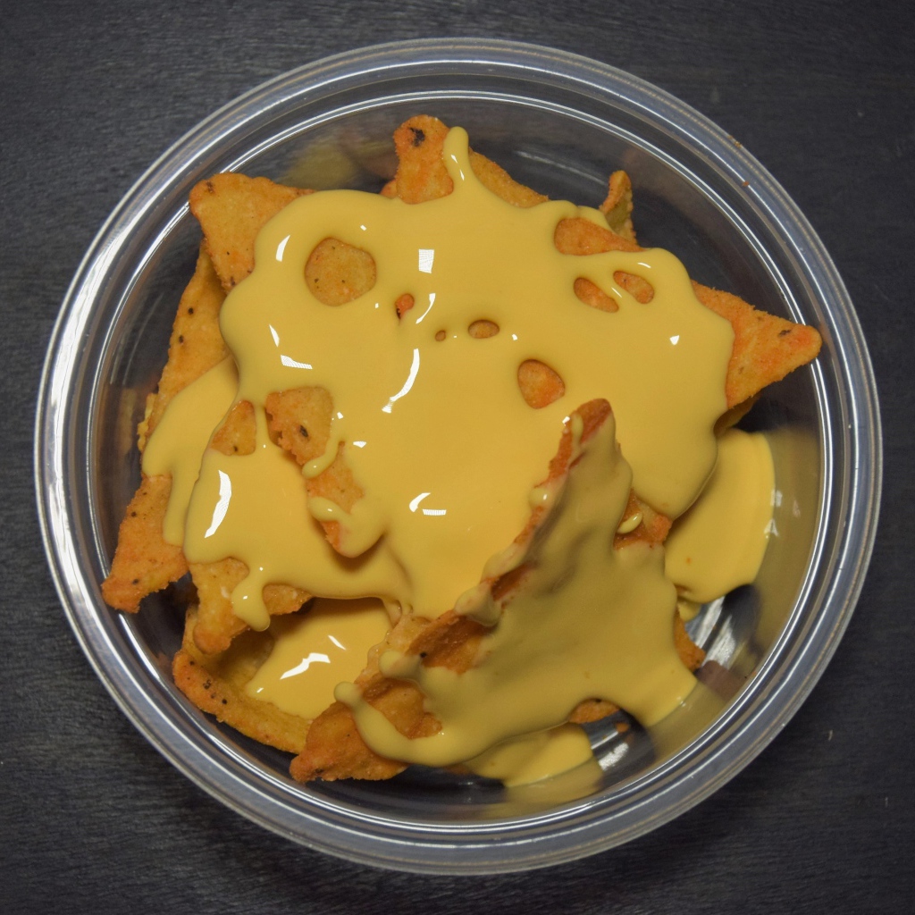 Чипсы начос с сырным соусом в миске на черном фоне