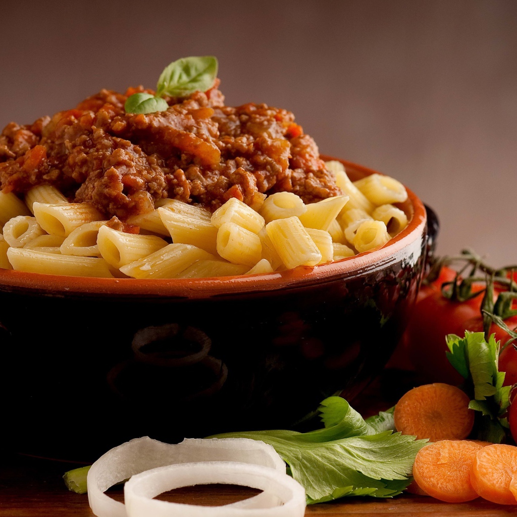 Макароны в миске с фаршем на столе с помидорами