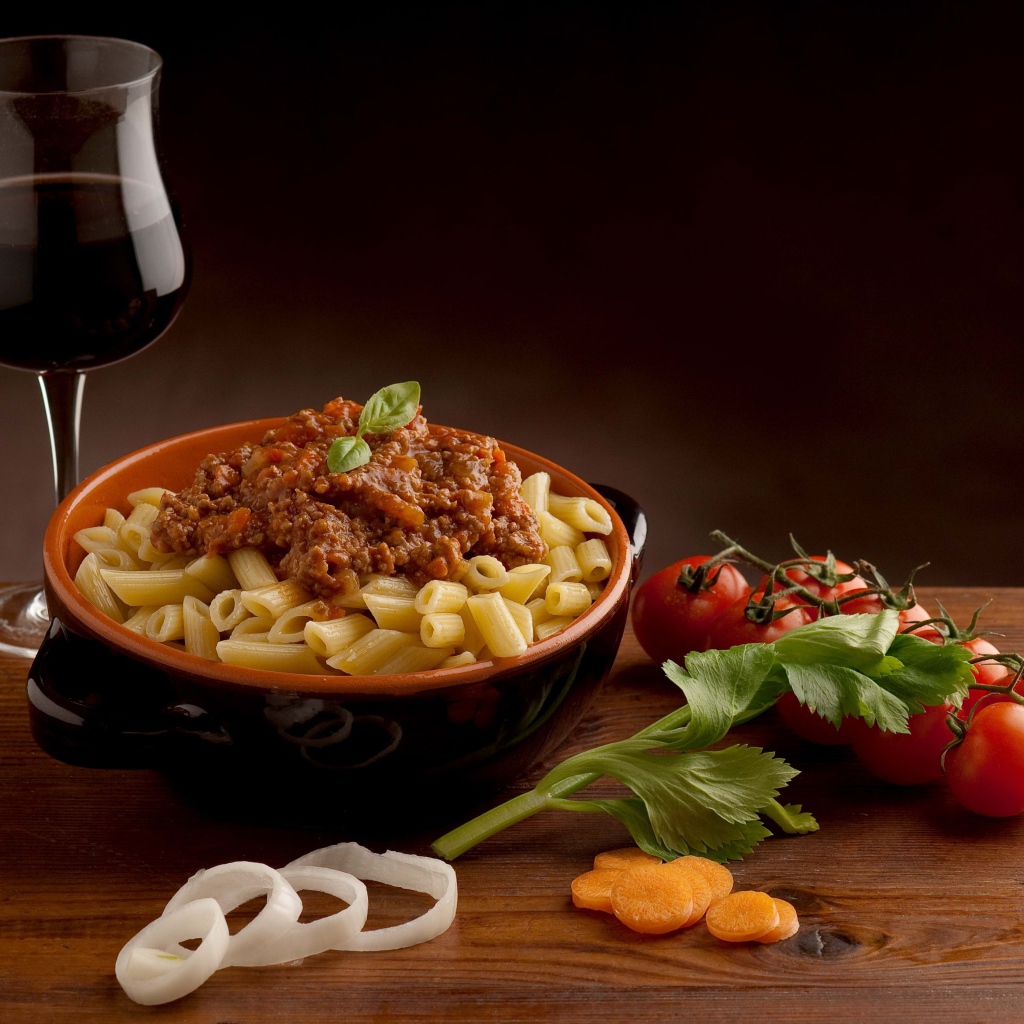 Макароны с фаршем на столе с бокалом вина и помидорами