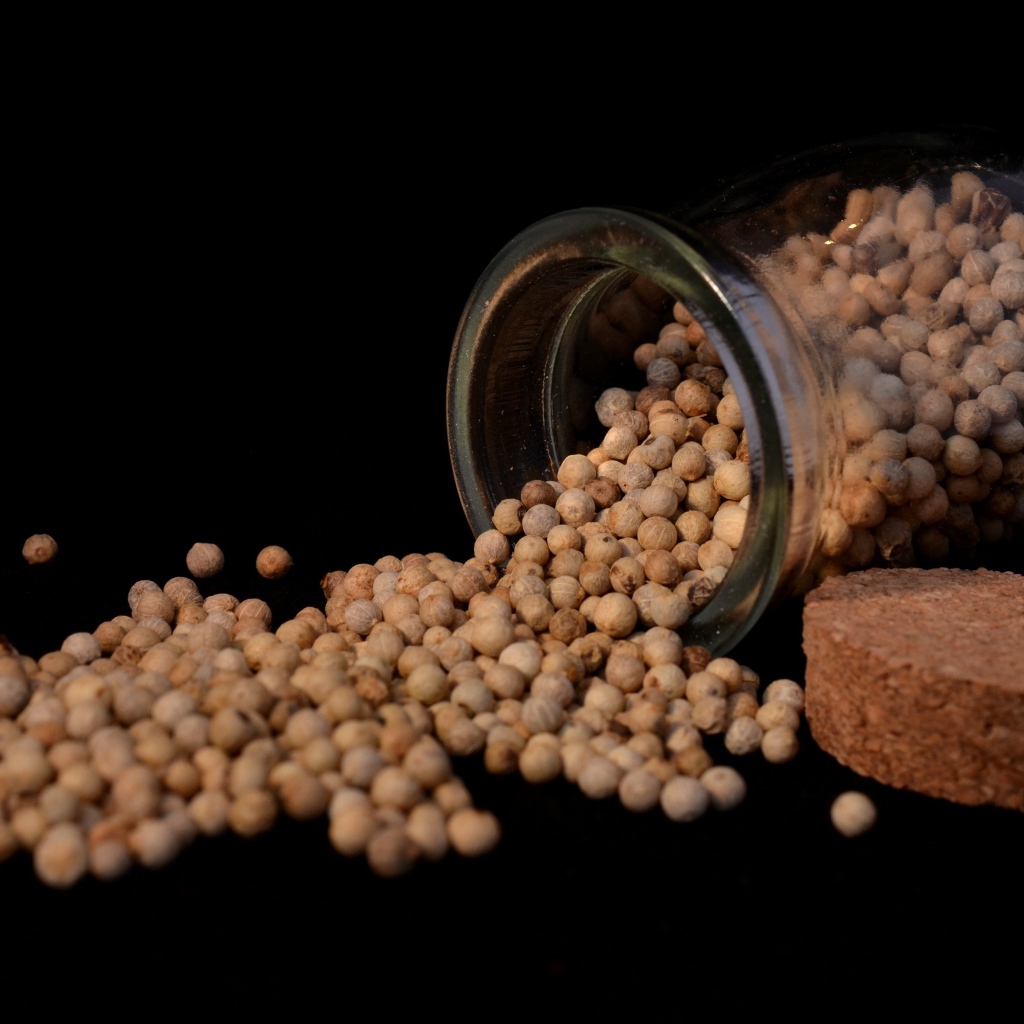 Перец горошек в стеклянной банке на черном фоне 