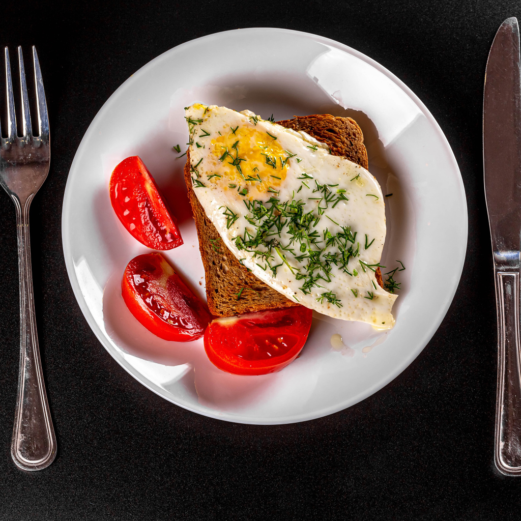 Кусок хлеба с яичницей на тарелке с помидорами