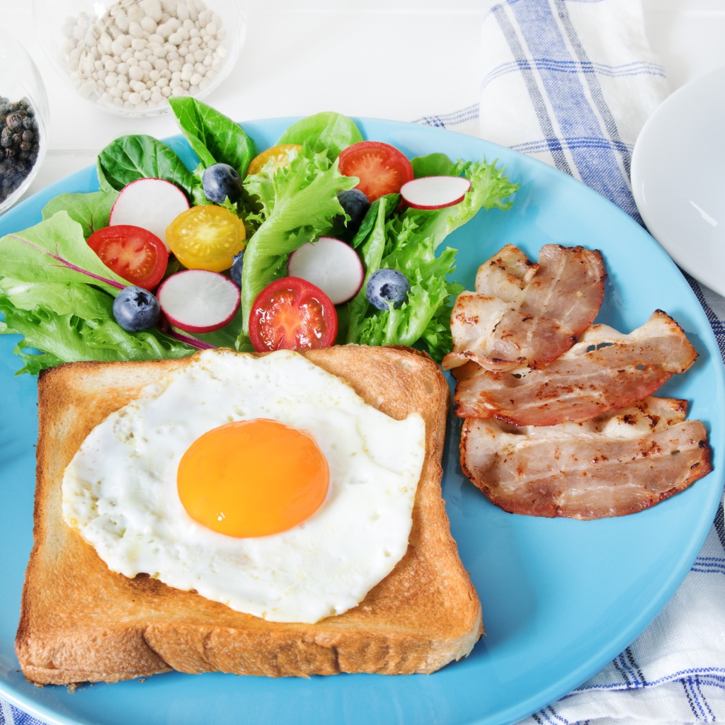 Яичница с хлебом на тарелке с салатом и беконом 