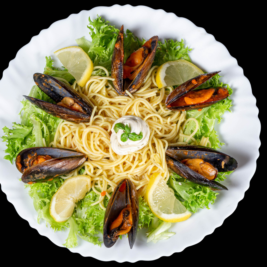 Спагетти с мидиями и листьями салата на белой тарелке