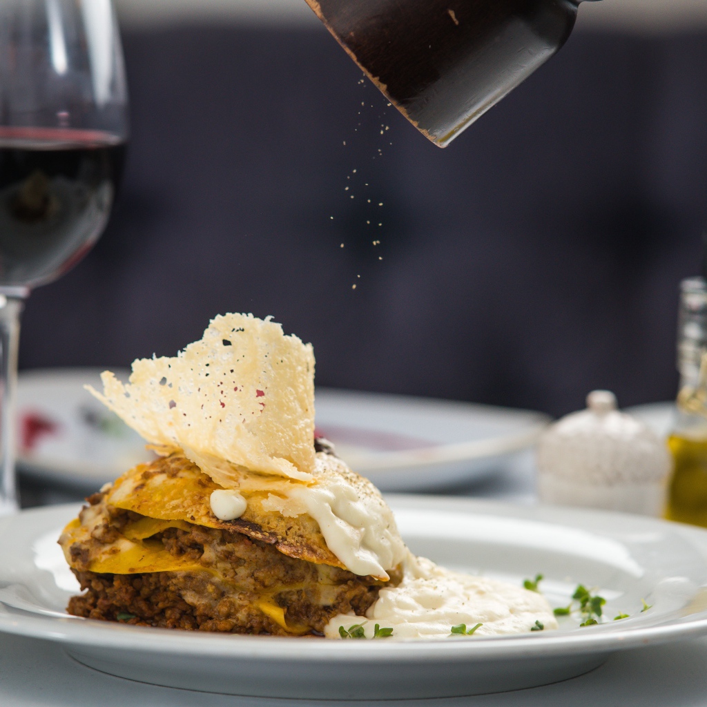 Кусок лазаньи посыпают перцем 