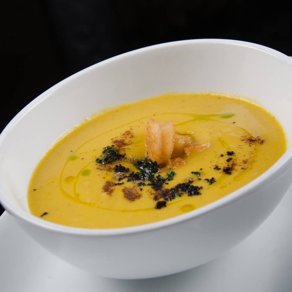 Желтый суп пюре в белой тарелке на черном фоне
