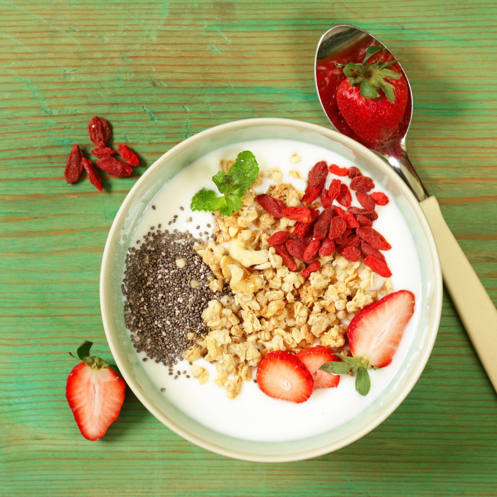 Йогурт с сухофруктами и клубникой на столе в миске 