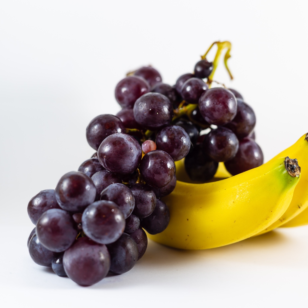 Гроздь розового винограда и бананы на белом фоне