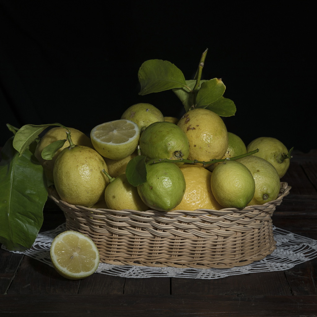 Лимоны и лаймы в плетеной корзинке на черном фоне