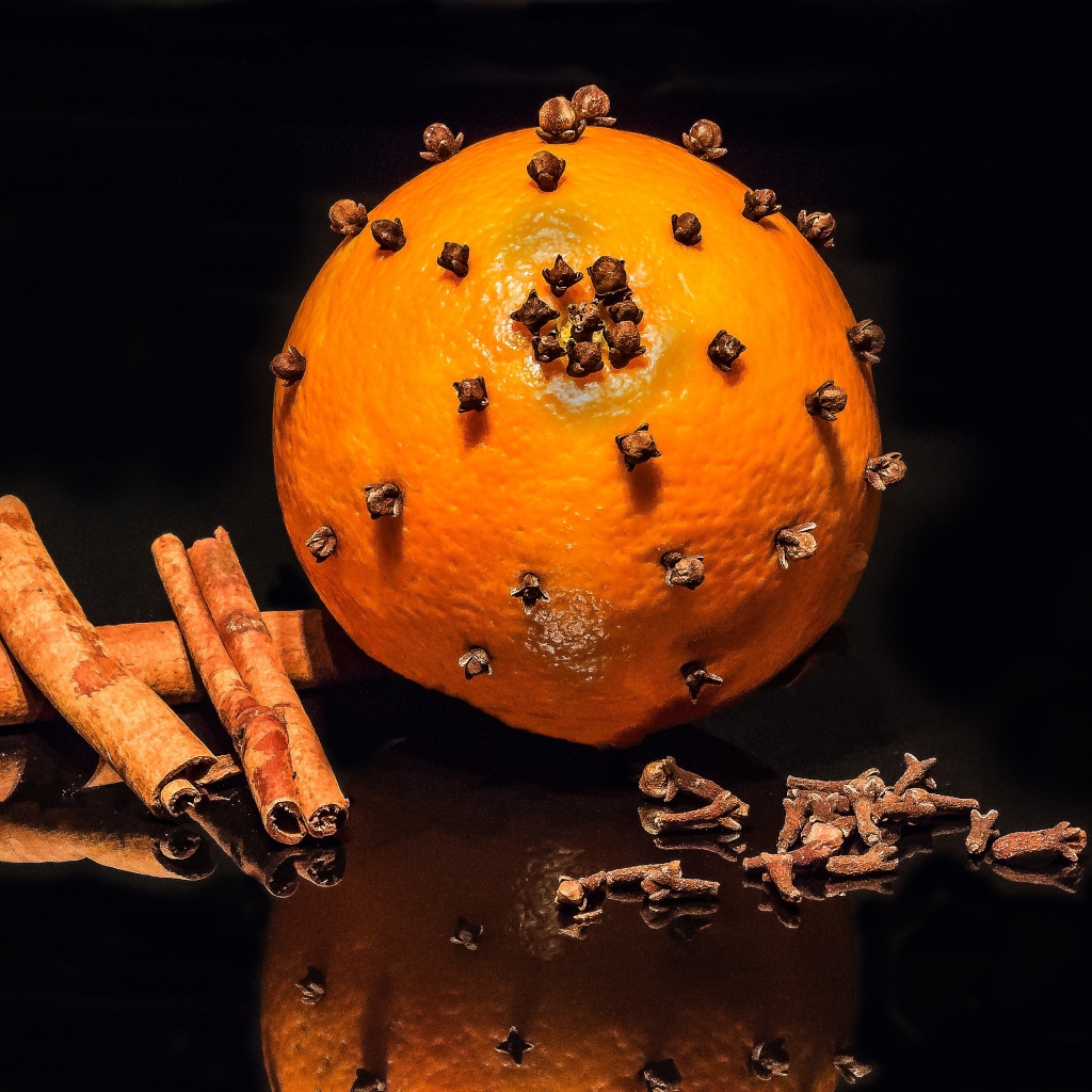 Оранжевый апельсин с гвоздикой и корицей на черном фоне 