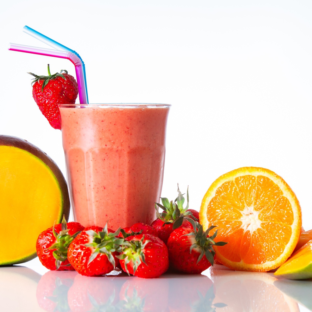 Спелое манго с клубникой и апельсином на столе со смузи