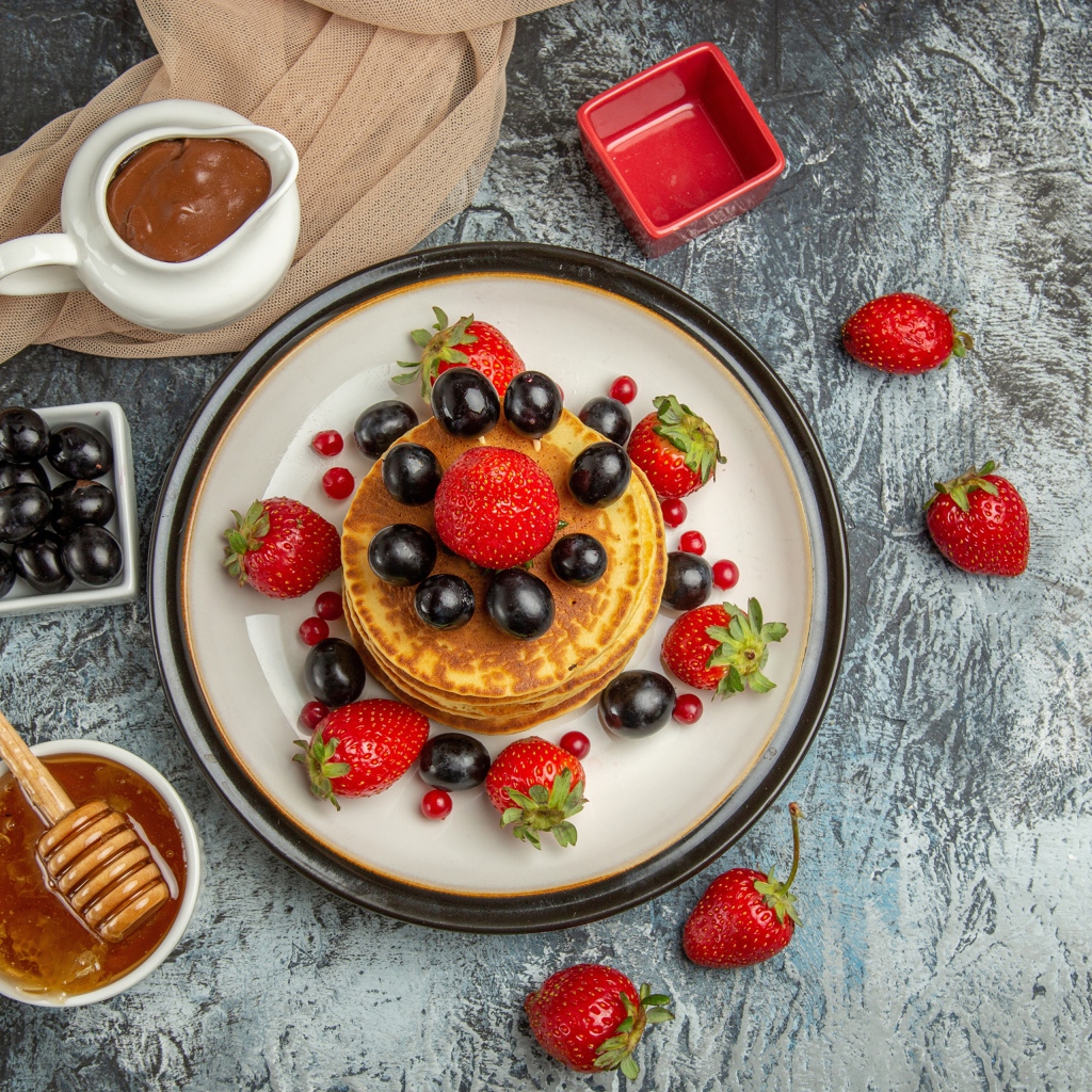 Оладьи с ягодами клубники и винограда на столе с медом