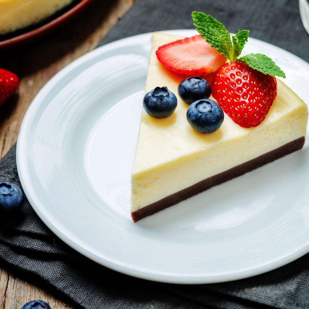 Кусок чизкейка на белой тарелке с клубникой и черникой 