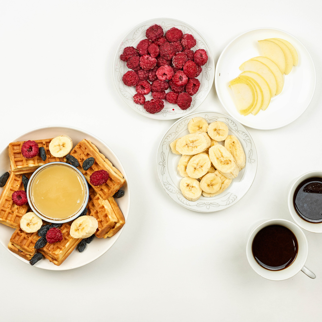 Сладкие вафли с малиной и бананами на столе  с кофе