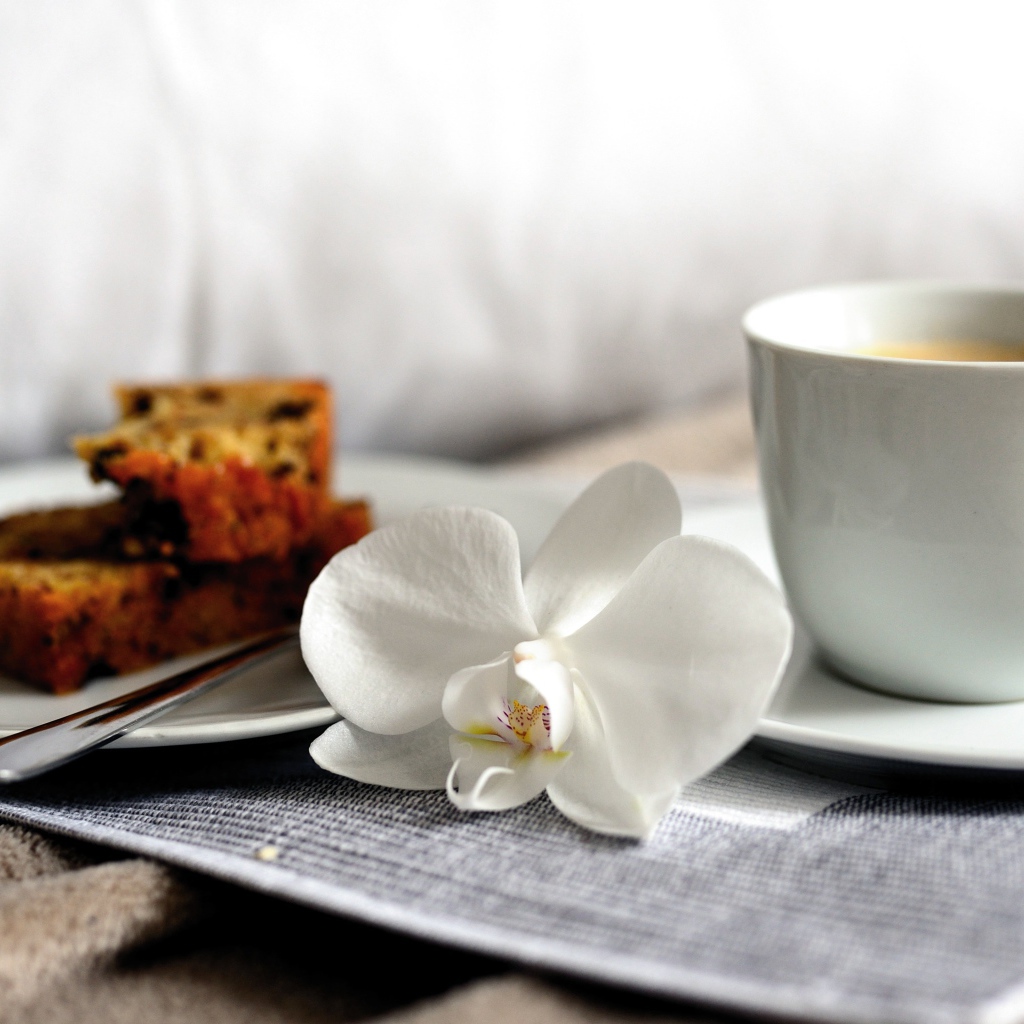 Чашка кофе на столе с цветком орхидеи и кусочками кекса 