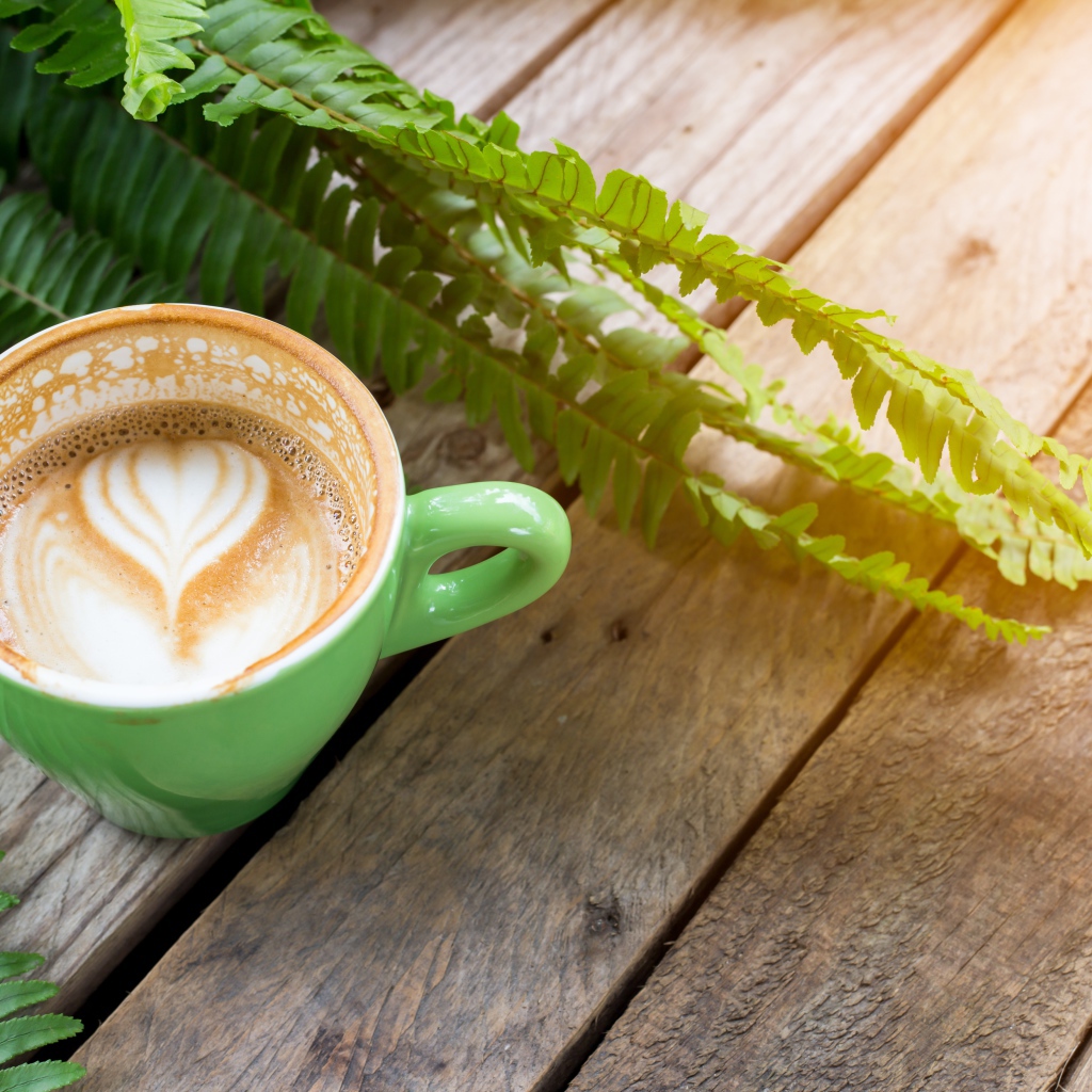 Чашка вкусного капучино  на столе с листьями папоротника