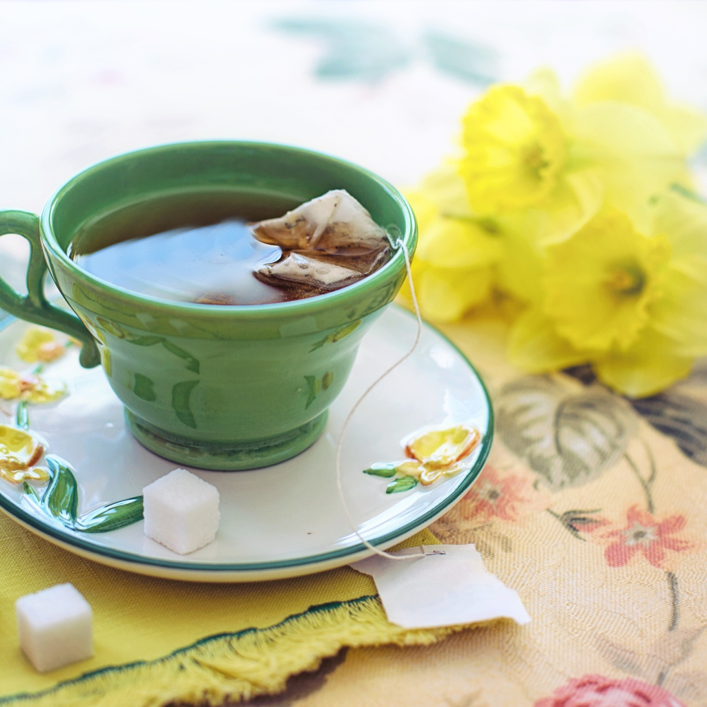 Чашка чая на столе с сахаром и нарциссами