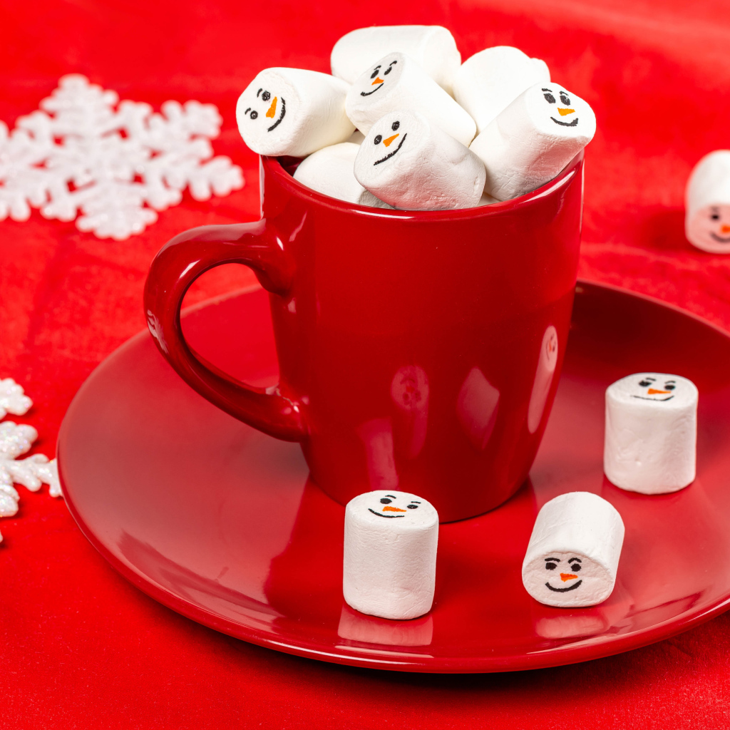 Красная чашка с маршмеллоу на столе со снежинками