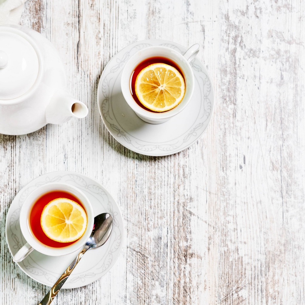 Две чашки чая с лимоном на столе с белым чайником