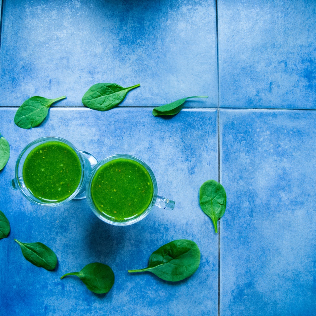 Два зеленых смузи с листьями базилика на голубом фоне